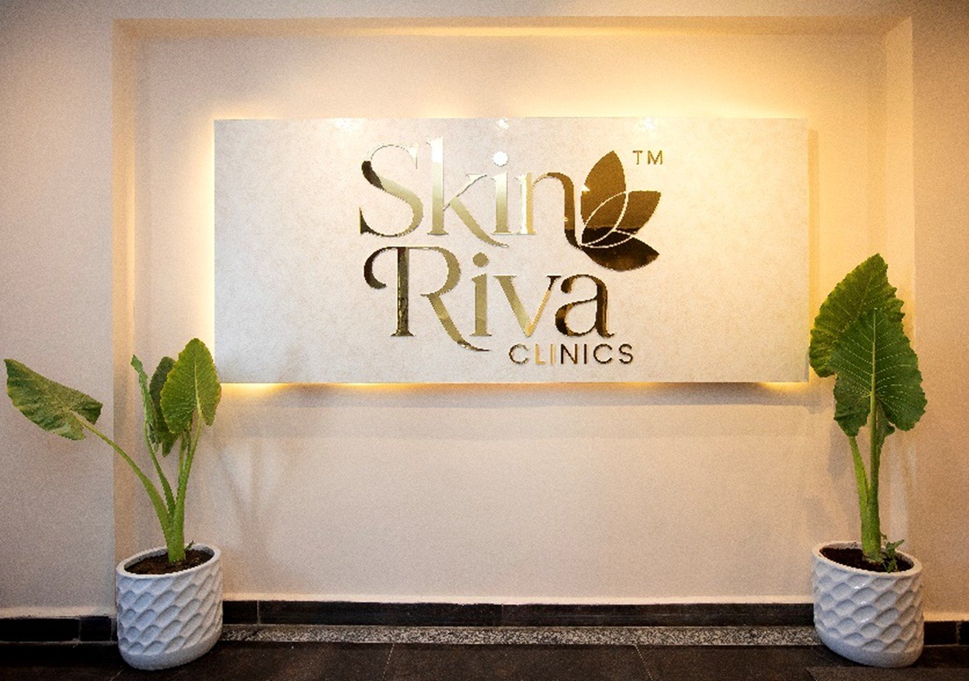 Skin Riva Clinics signature backlit gold logo on marble wall with planters